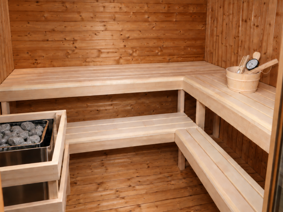Interieur van de Passion Cube Luxury 300 Multiroom sauna met houten hoekbanken op twee hoogtes en een kachel met stenen.