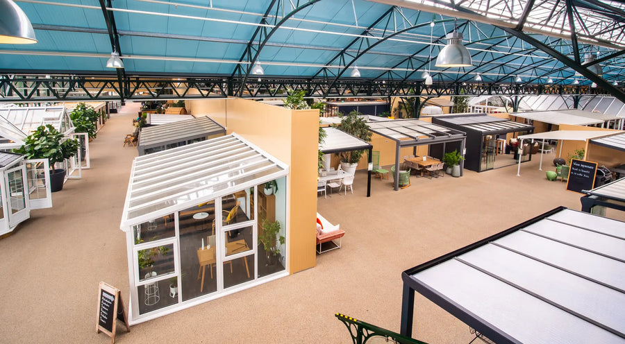 Overzicht van tuinhuizen en overkappingen onder de glazen kap van een showroom.